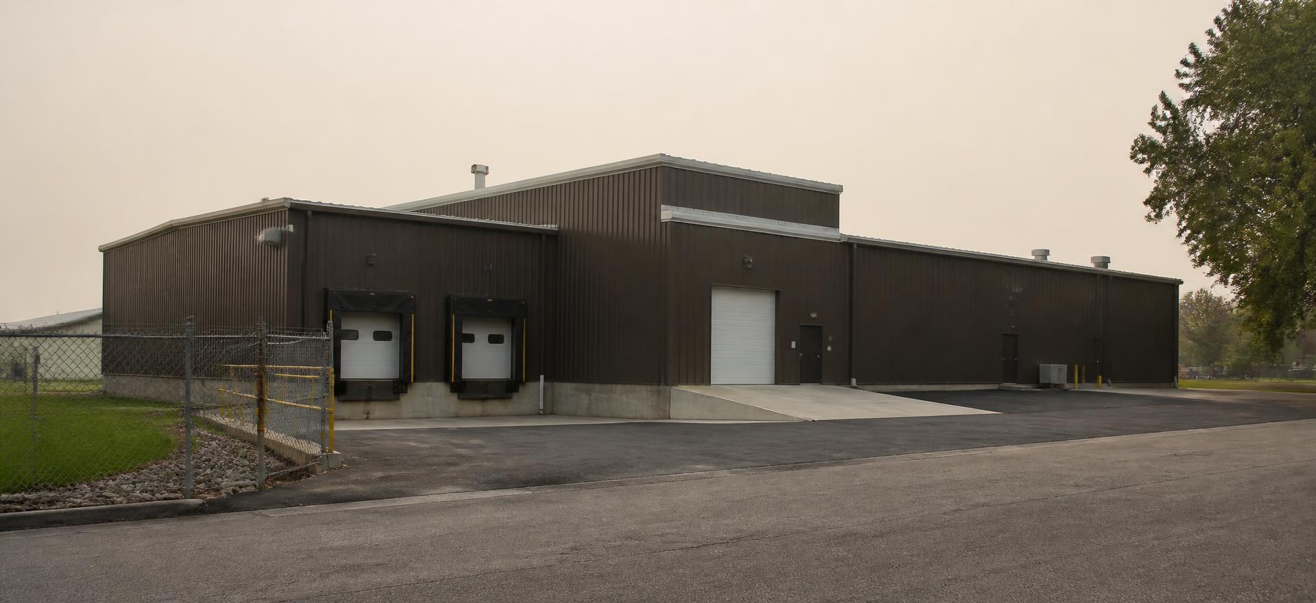 Concept photograph of a dark bronze steel industrial building with two dock doors, a concrete ramp and a drive-in door behind a chain-link fence; example configuration, not a real project.