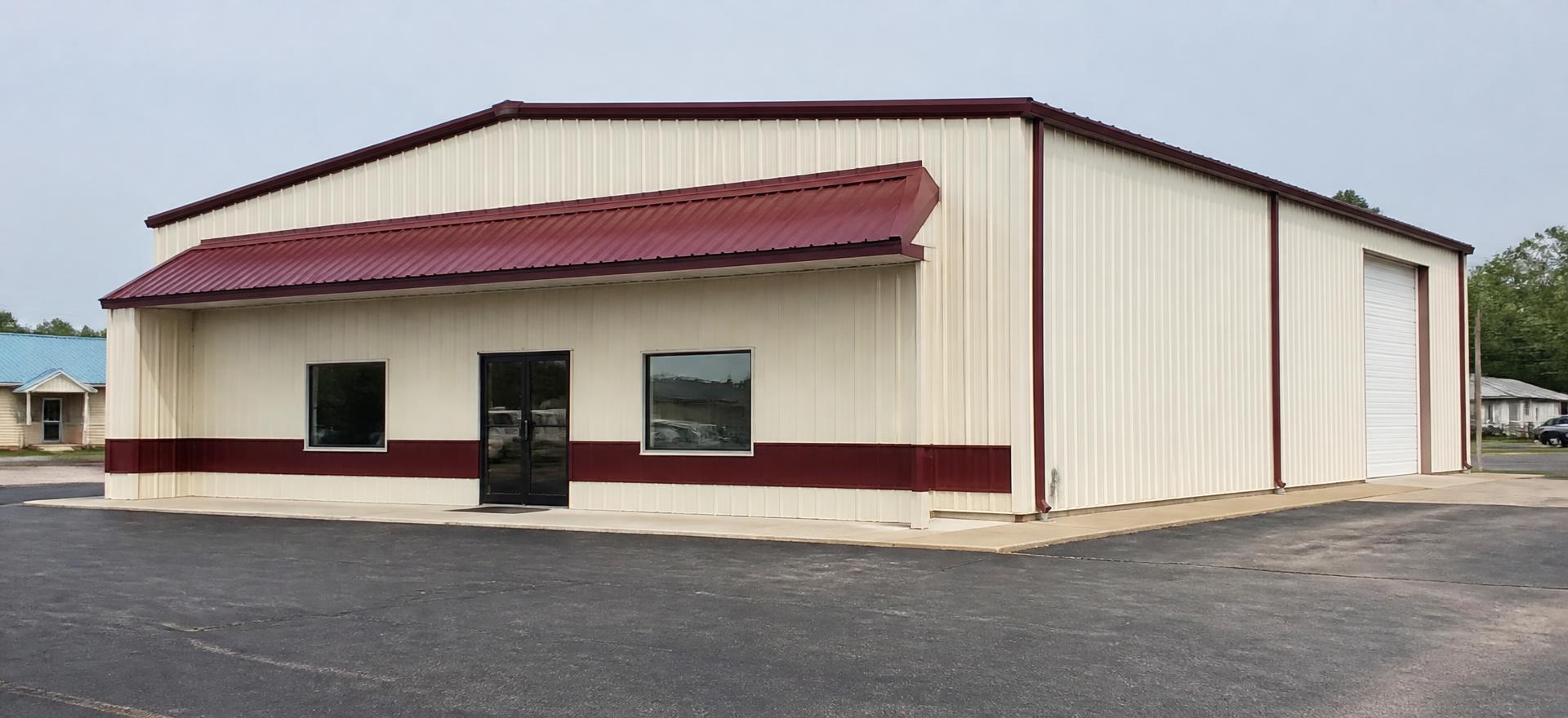 Concept photograph of a cream steel office and warehouse building with a burgundy canopy, glass entry and a side roll-up door; example configuration, not a real project.