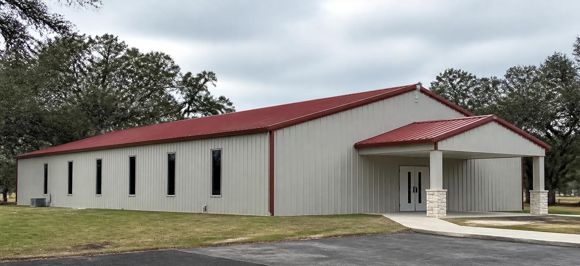 Concept photograph of a grey steel assembly building with a red roof, gabled entry canopy on stone piers and tall narrow side windows; example configuration, not a real project.