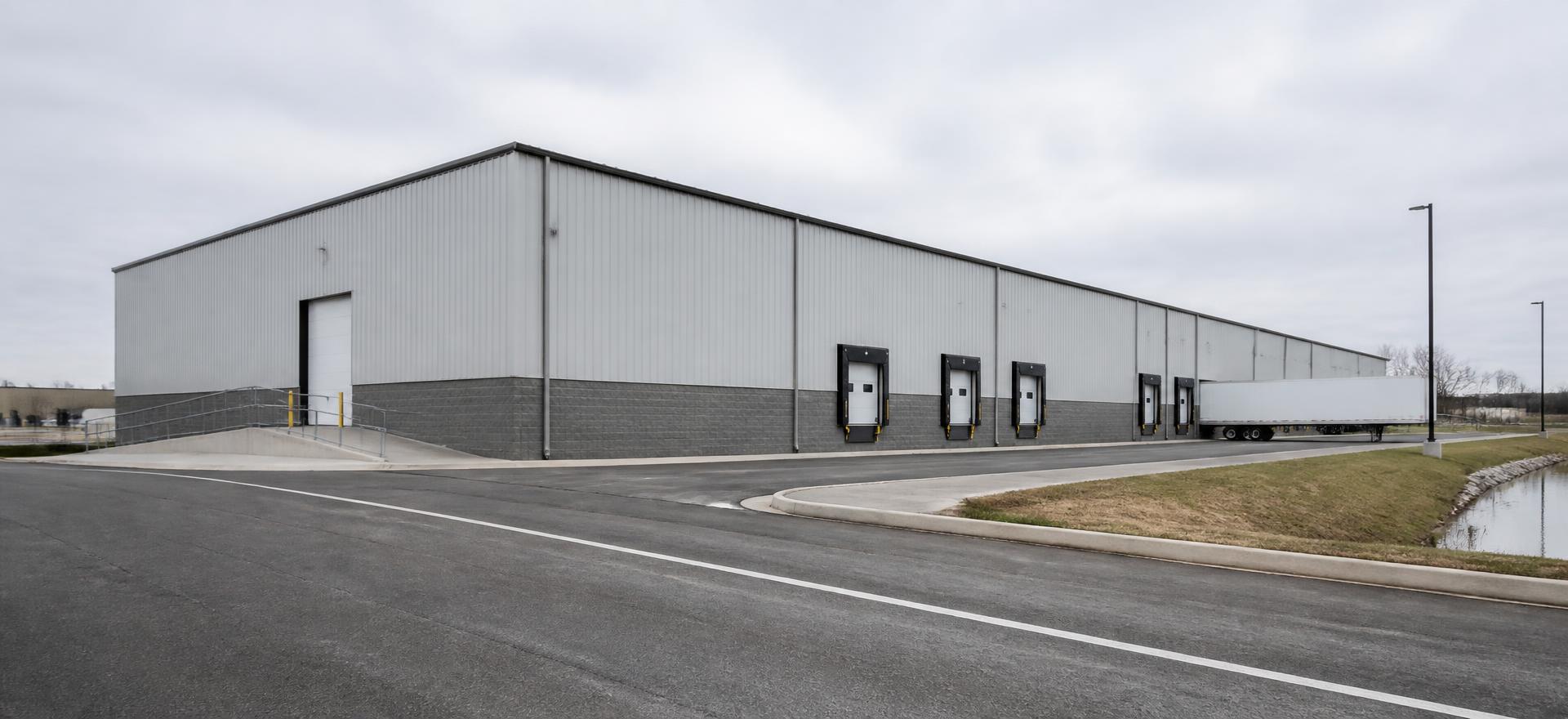 Concept photograph of a 100 by 200 foot pre-engineered steel distribution building with four loading docks, a ramped drive-in door and a concrete truck court; example configuration, not a real project.