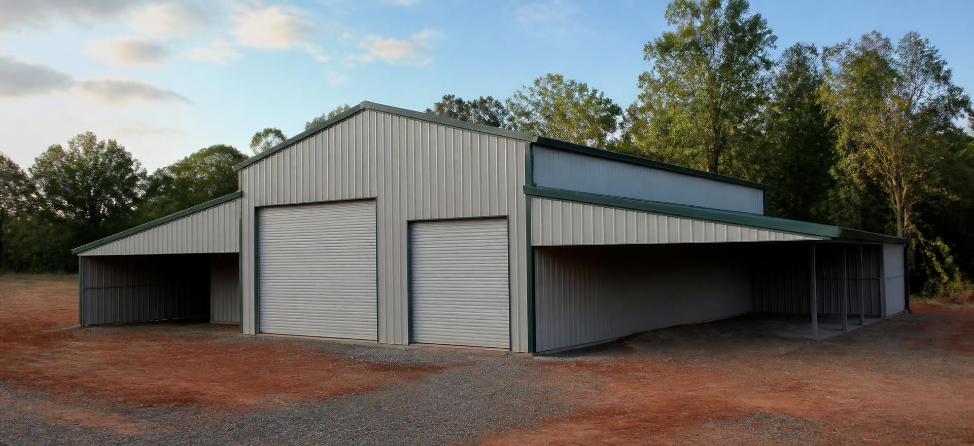 Concept photograph of a grey barn-style steel building with a raised centre section, two roll-up doors and open side sheds on a gravel pad; example configuration, not a real project.