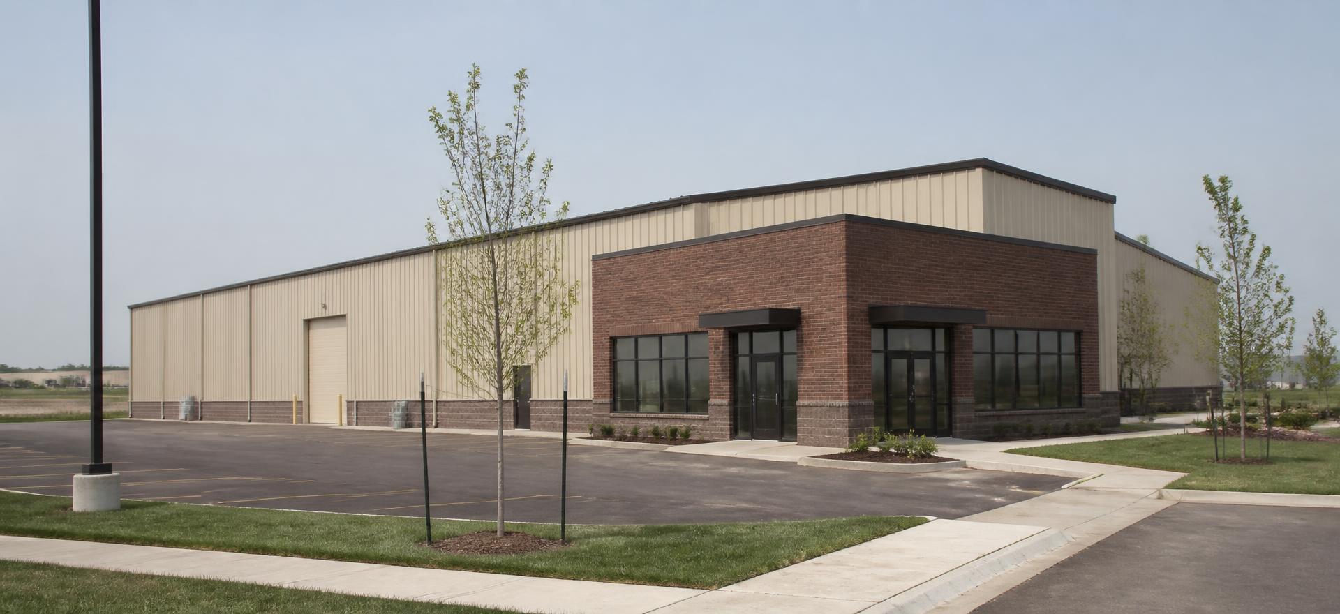 Concept photograph of a tan steel commercial building with a brick-faced entry element, glazed doors and a side roll-up door; example configuration, not a real project.