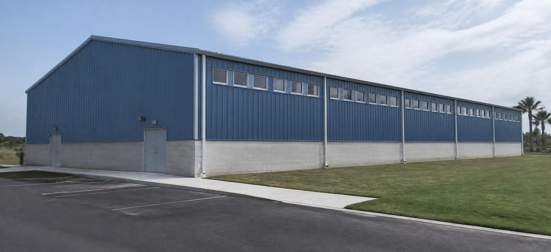 Concept photograph of a blue steel sports building with a masonry base, a band of high clerestory windows and plain double entry doors; example configuration, not a real project.