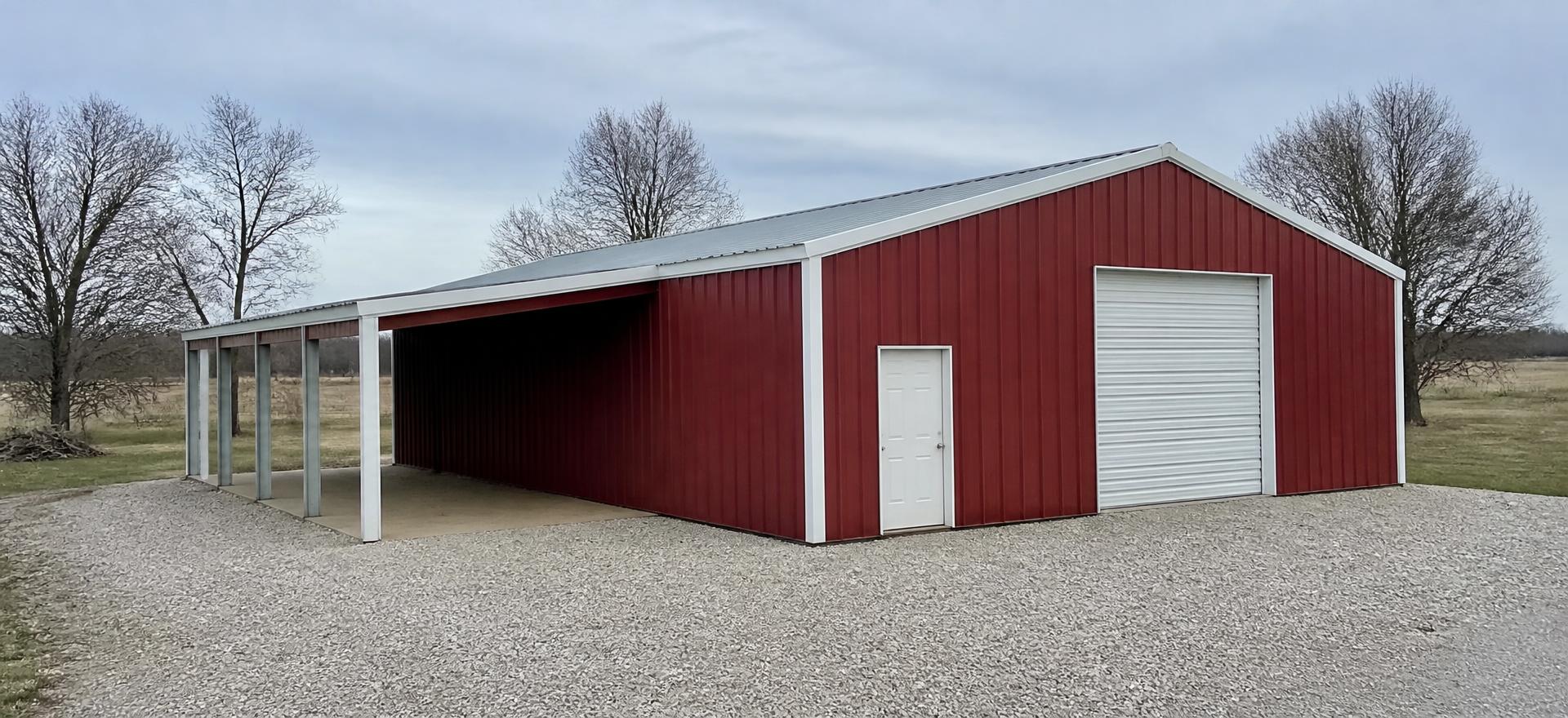 Concept photograph of a red steel garage with a white-trimmed roll-up door and an attached open lean-to bay on a gravel drive; example configuration, not a real project.