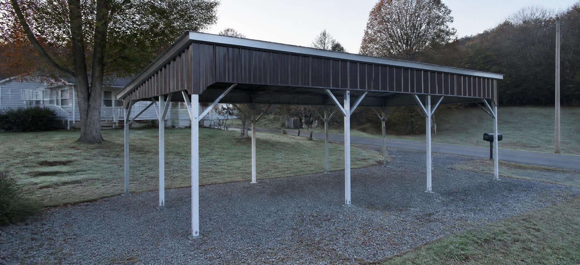 Concept photograph of an open brown-roofed tube-frame steel carport on a gravel pad beside a small house on a frosty morning; example configuration, not a real project.