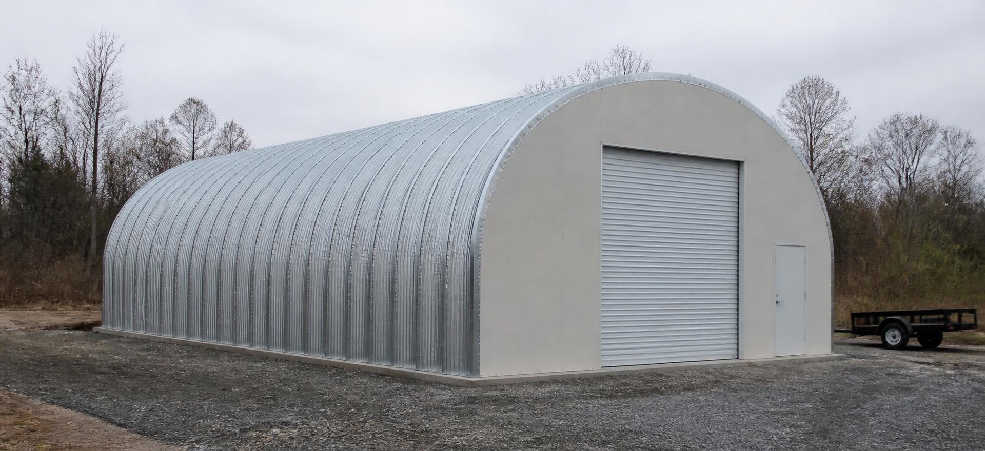 Concept photograph of a 30 by 50 foot galvanized corrugated steel arch building with a sheeted front end wall, roll-up door and walk door on a concrete perimeter footing; illustrative configuration, not a real project.