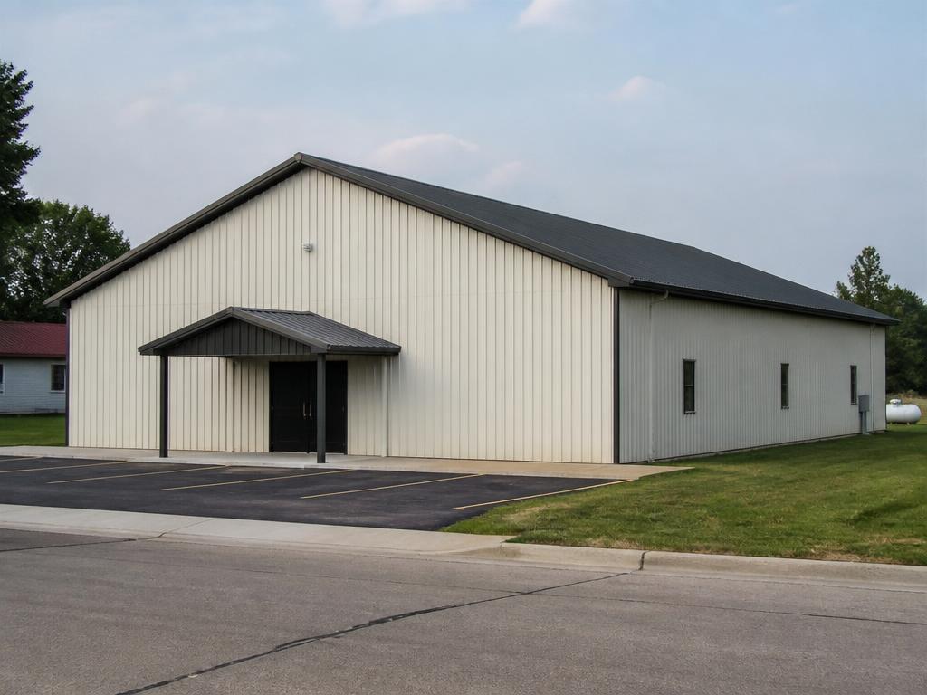 Concept photograph of an off-white steel assembly hall with a small covered entry canopy and a paved parking area; example configuration, not a real project.