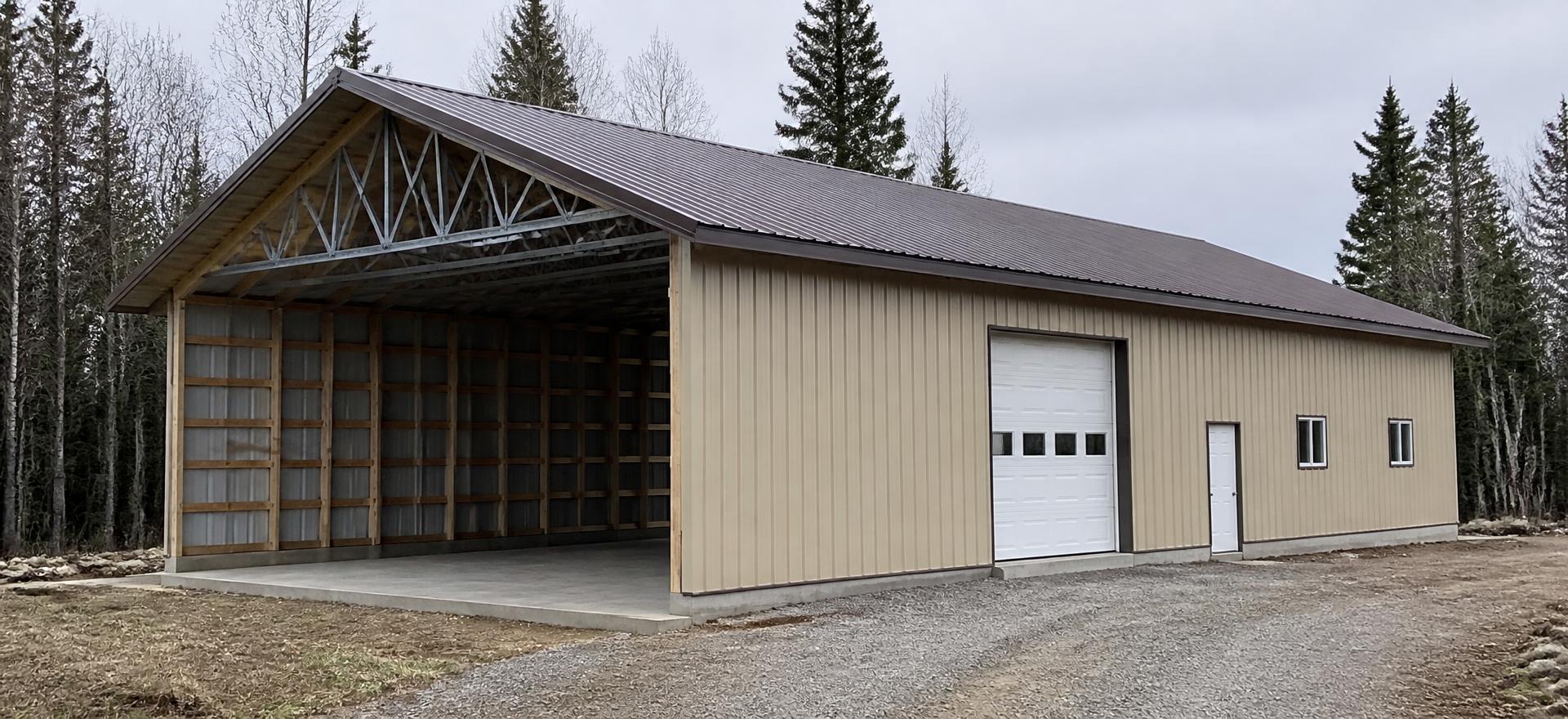 Concept photograph of a 40 by 60 foot hybrid building with exposed galvanized steel web trusses over wood framing at an open end bay, beige ribbed steel siding, a bronze gable metal roof and an overhead door; illustrative configuration, not a real project.