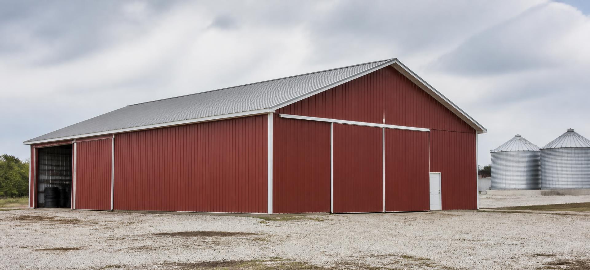 Concept photograph of a large red post-frame barn clad in steel with white trim, sliding doors and grain bins behind; example configuration, not a real project.
