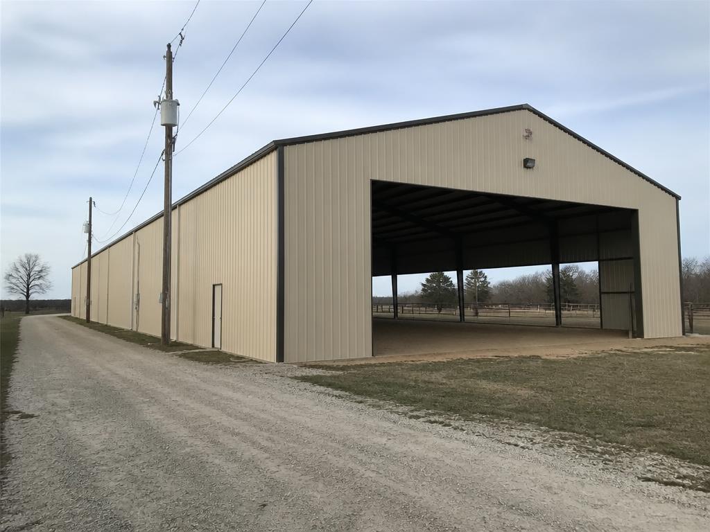 Concept photograph of a beige steel riding arena with a tall open gable-end bay showing sand footing inside; example configuration, not a real project.