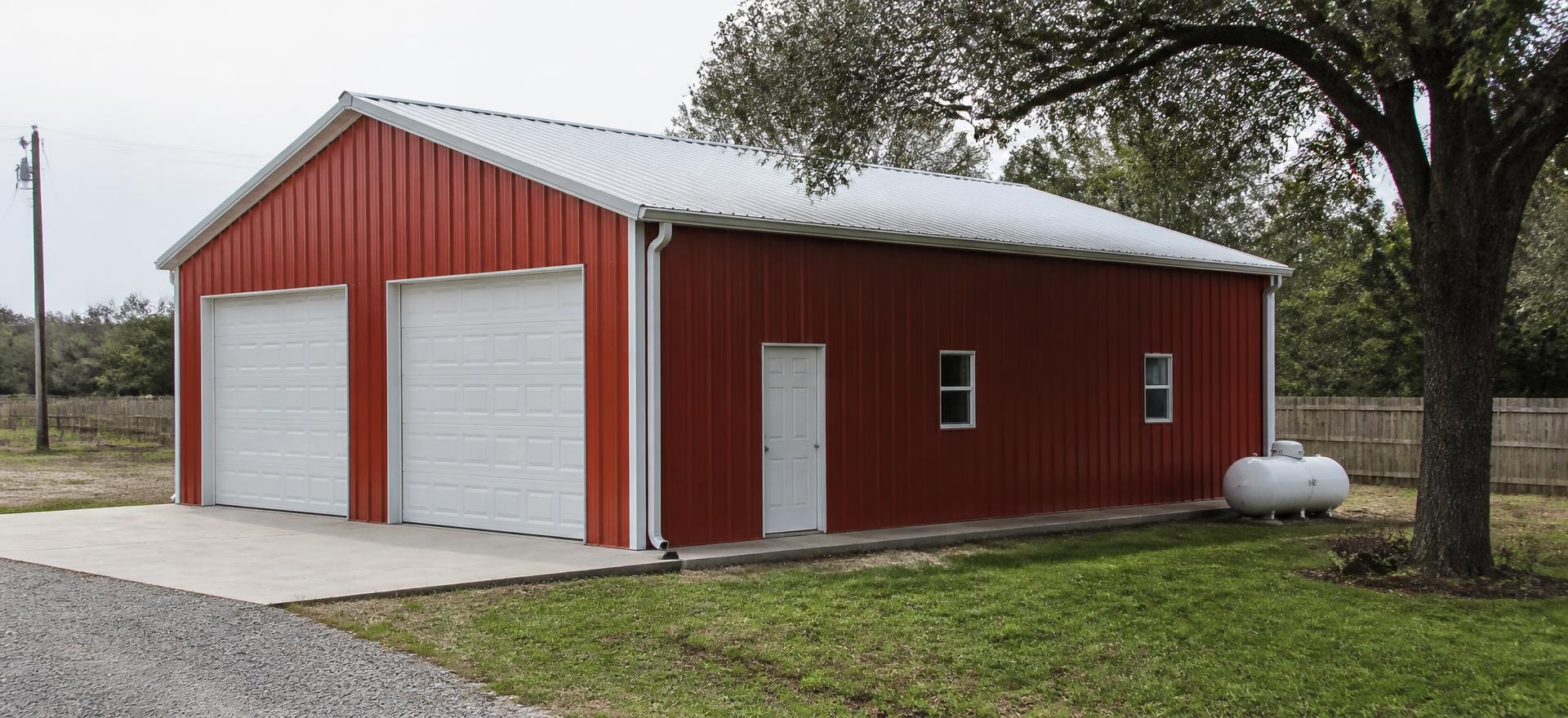 Concept photograph of a 30 by 40 foot red steel garage and workshop with two white overhead doors, a walk door and a galvalume roof on a rural lot; example configuration, not a real project.