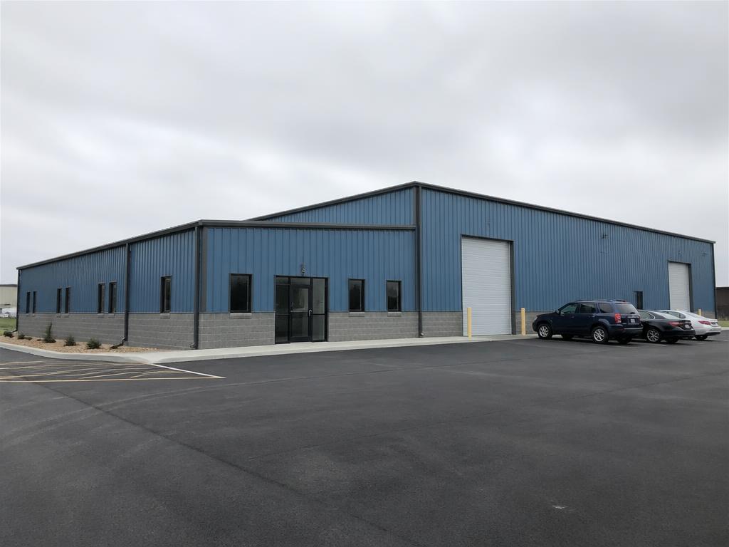 Concept photograph of a blue steel industrial building with a glazed office entrance and two service doors on an asphalt lot; example configuration, not a real project.