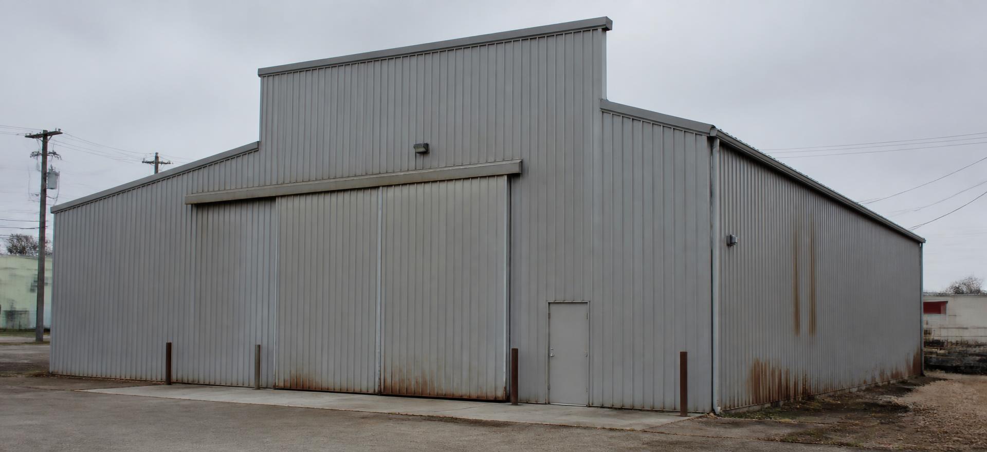 Concept photograph of a weathered grey steel industrial building with a tall clear-span bay and a wide sliding industrial door; example configuration, not a real project.