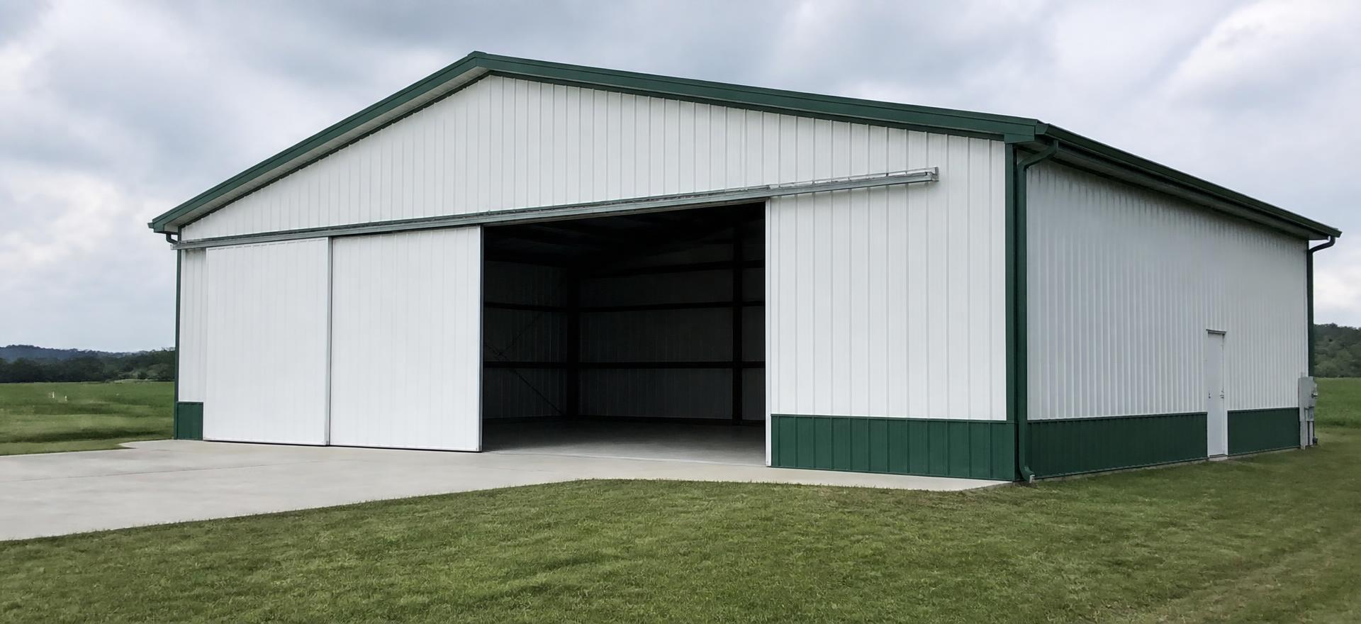 Concept photograph of a white steel hangar with green trim and a wide sliding hangar door partly open showing a tall clear opening onto a concrete apron; example configuration, not a real project.