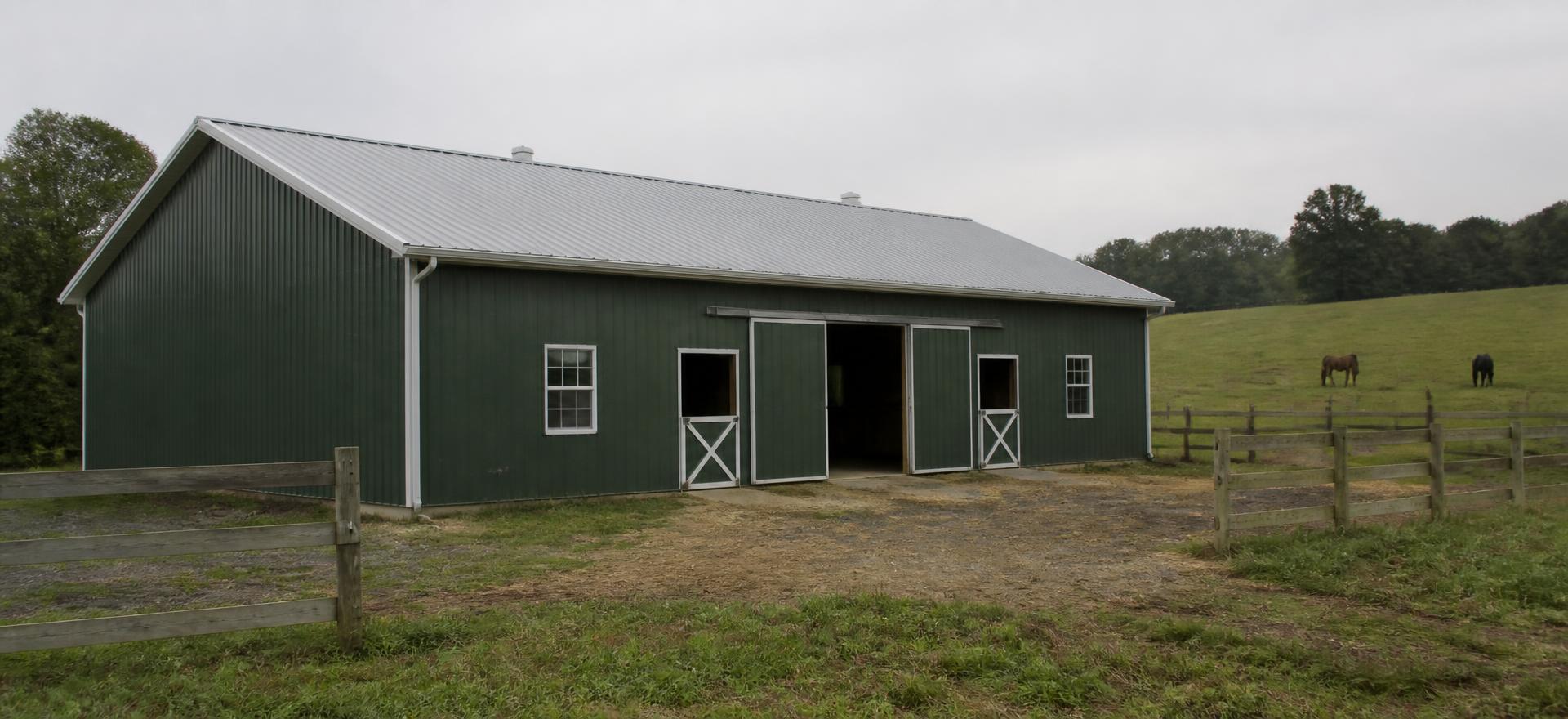 Concept photograph of a 40 by 72 foot dark green post-frame horse barn with white trim, a light grey gable metal roof, centre sliding doors, dutch stall doors and windows beside a fenced pasture; illustrative configuration, not a real project.