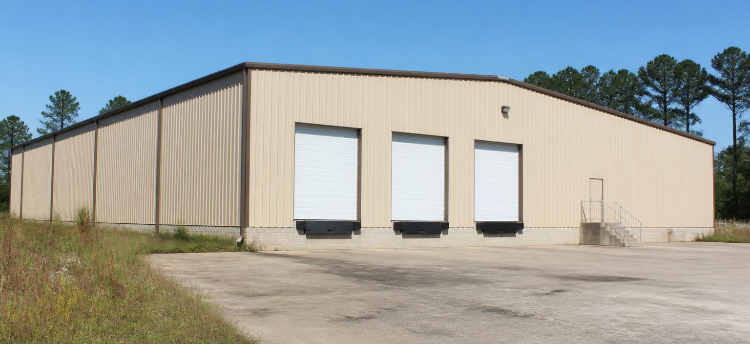 Steel building configuration showing a beige pre-engineered warehouse with three dock doors, dock bumpers and a steel stair on a stained concrete truck apron.